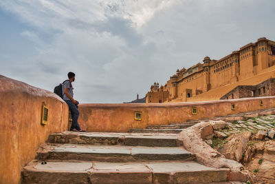 Tourist standing on staircase in fort against cloudy sky