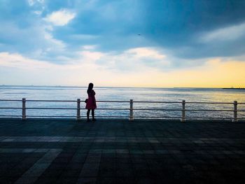 Rear view of woman looking at sea against cloudy sky during sunset