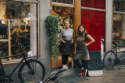 Full length portrait of young woman with bicycle standing against graffiti