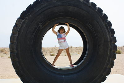 Full length of girl standing with arms raised in tire