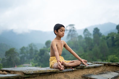 Full length of shirtless boy sitting on mountain