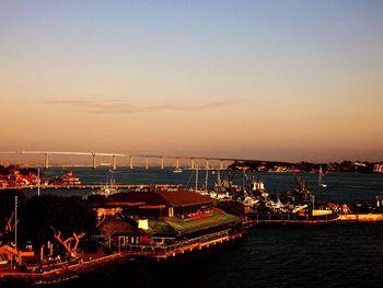 High angle view of illuminated city by sea against sky during sunset