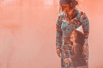 Woman with happy daughter standing against wall