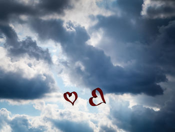 Low angle view of heart shape kites flying against cloudy sky