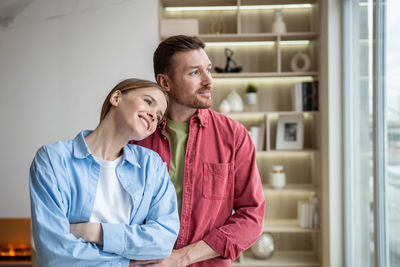Romantic loving couple standing in front of window, dreaming, thinking of future plans, children