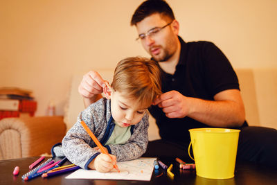 Father holding son ear making drawing on table at home