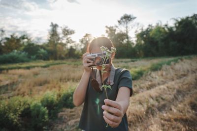 Woman photographing plant while standing on field