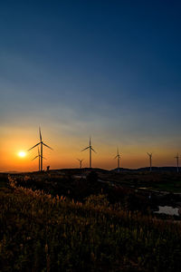 Silhouette of wind turbines on field against sky during sunset