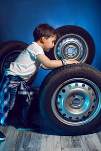 Boy in a white t shirt shirt and hat sits on a background of car wheels on a blue