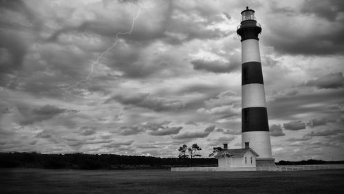 Lighthouse on field by building against sky