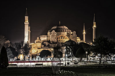 Illuminated mosque in city against sky at night