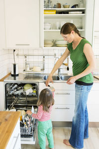 Full length mother taking spoon from little daughter in kitchen