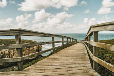 Wooden pier leading towards sea against sky