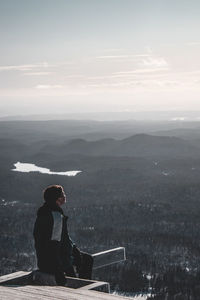 Side view of man sitting against sky during winter