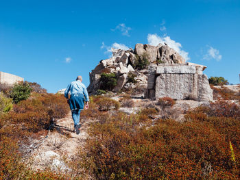 Rear view of man standing on rock against sky