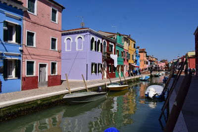 Boats moored in canal by buildings in city against clear sky