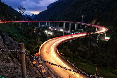 Light trails on road by bridge against mountain