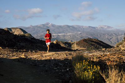 Rear view of man walking on mountain against sky