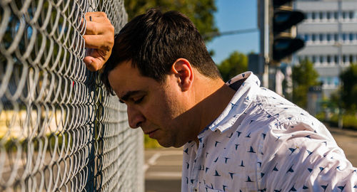 Depressed man standing by chainlink fence