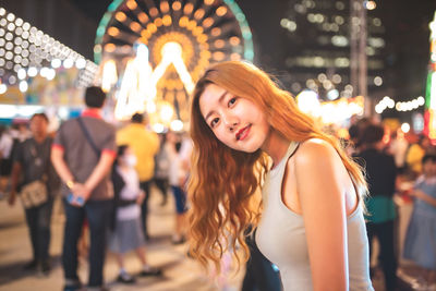 Portrait of smiling young woman standing against illuminated lights