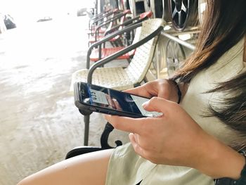 Midsection of woman using mobile phone while sitting on chair