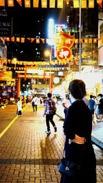 Rear view of people walking on illuminated street at night