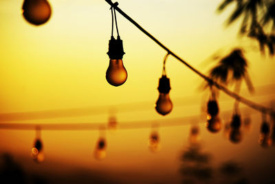 Close-up of light bulbs hanging against sky during sunset