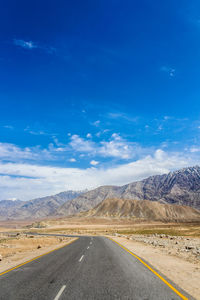 Road leading towards mountains against blue sky