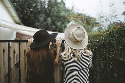 Rear view of friends peeping through fence in yard