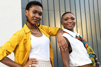 Confident young black female friends with short dark hair in stylish clothes standing on street and looking at camera on sunny day