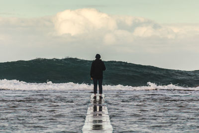 Rear view of man standing on groyne over sea against sky