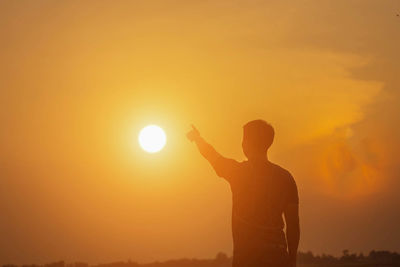 Silhouette man standing against orange sky during sunset