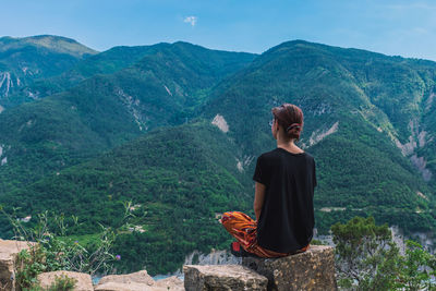 Rear view of woman sitting on mountain looking at mountains