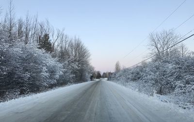 Empty road amidst snow covered trees against clear sky