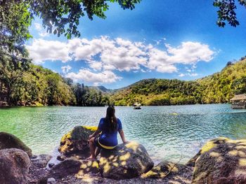 Man sitting on rock by lake against sky