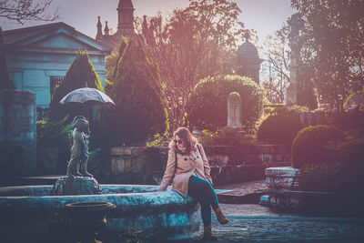 Portrait of woman sitting by building against trees