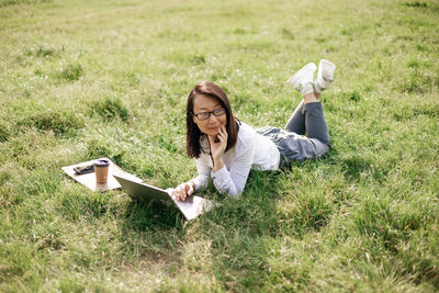 Young woman using laptop while sitting on grassy field