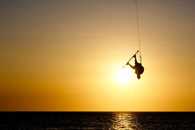 Silhouette kitesurfer hanging against sky during sunset