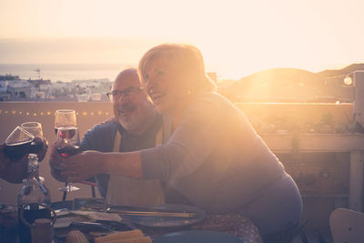 Smiling senior couple toasting drink at table in restaurant during sunset