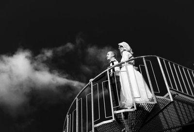 Low angle view of bridal couple standing on staircase against sky