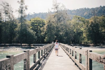 Rear view of woman standing on railing by trees