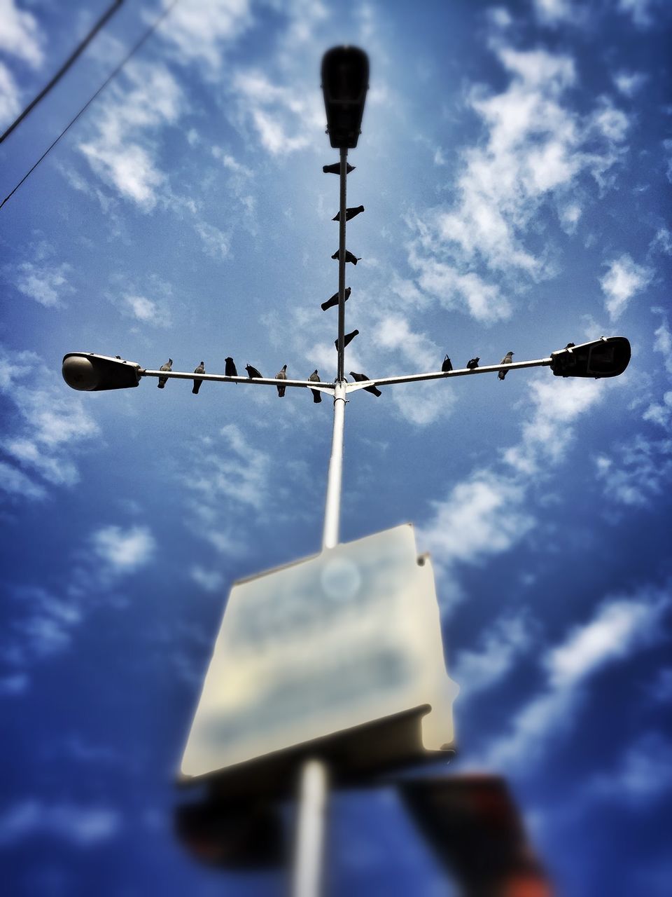 low angle view, sky, communication, lighting equipment, text, cloud - sky, hanging, street light, guidance, cloudy, western script, cloud, blue, road signal, pole, no people, outdoors, metal, technology, safety