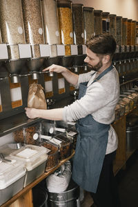 Side view of owner filling food in scoop while working in store