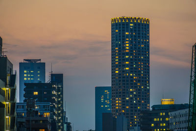 Illuminated buildings in city against sky at sunset