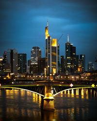 Illuminated bridge over river by buildings against sky at night