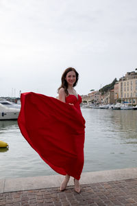 Portrait of woman in red dress standing against canal in city