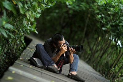 Man photographing while sitting by tree