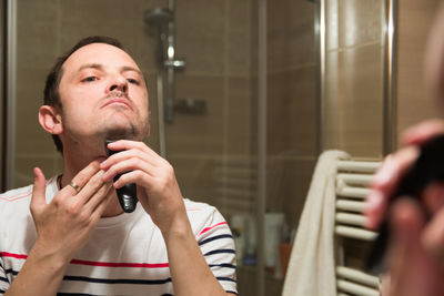 Reflection of man on mirror while trimming beard in bathroom