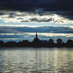 Silhouette of building by river against cloudy sky