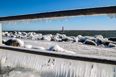 Close-up of icicles on railing by sea against clear blue sky